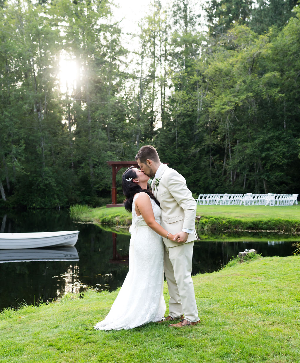 newlyweds kissing in front of the pond with a white rowboat in the background