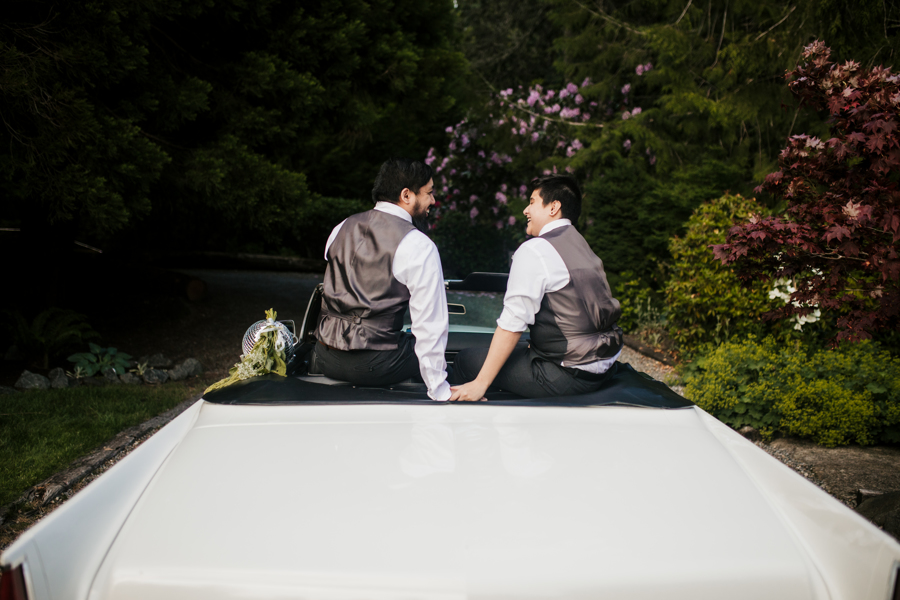 Newlyweds holding hands in the back of a convertible car as they exit to their honeymoon