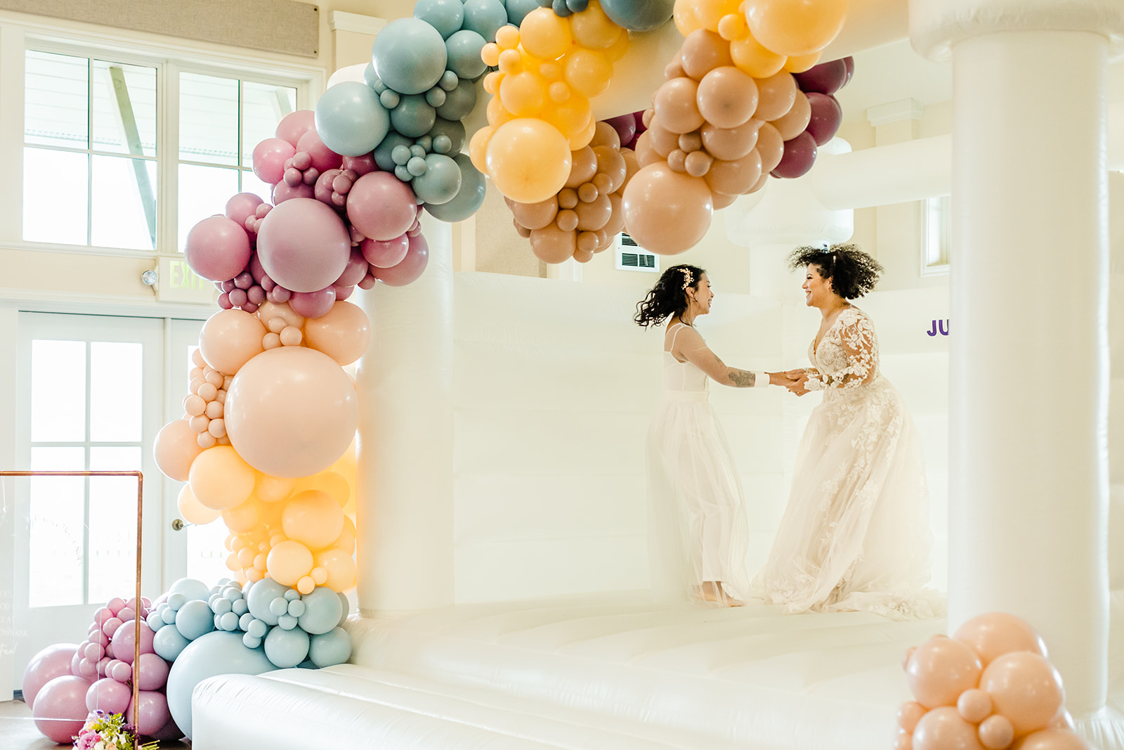 newlywed brides bouncing in a white bounce house on their wedding day