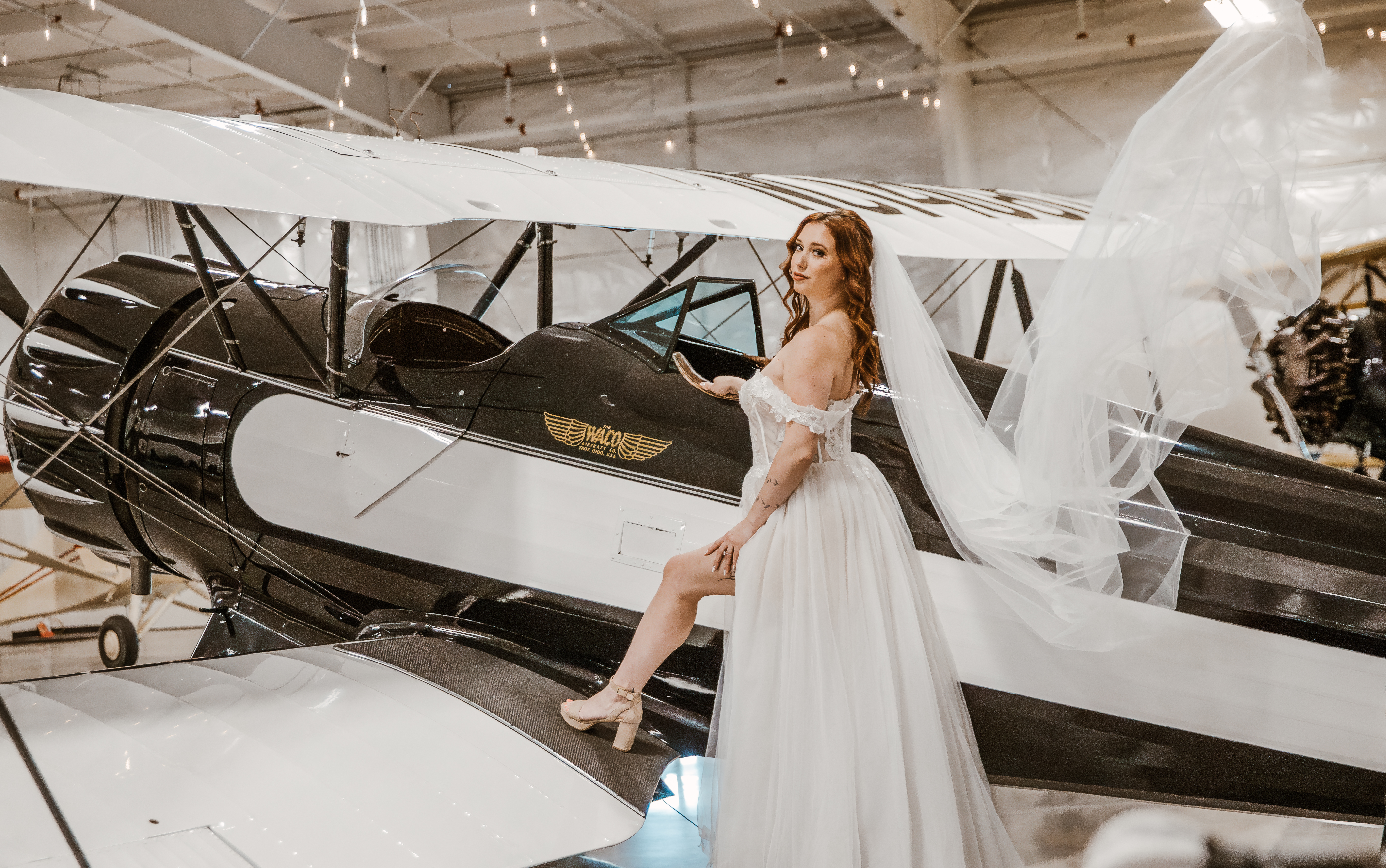 bride standing next to a vintage airplane in her wedding dress at the gig harbor aero museum
