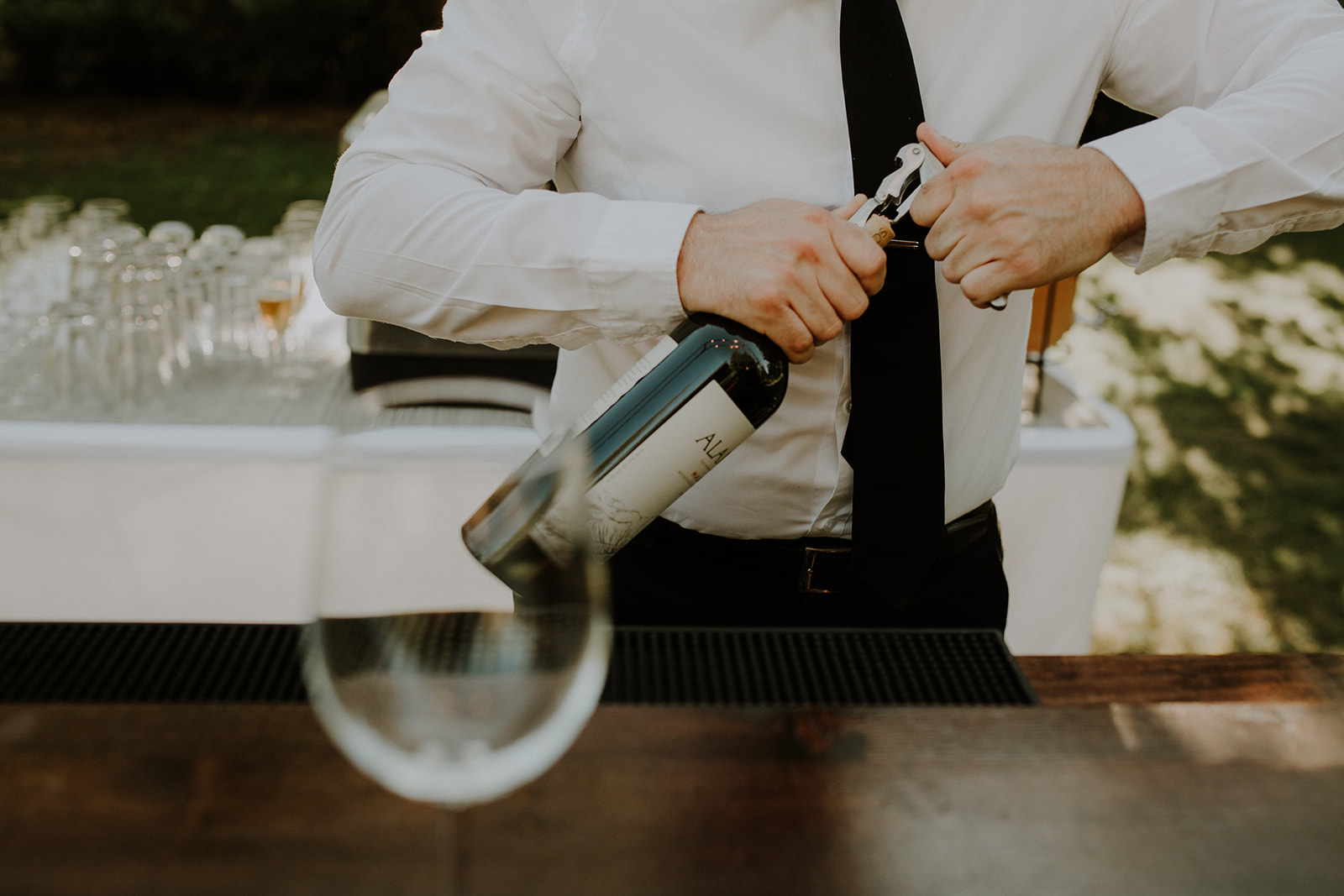 bartender opening a bottle of wine, with a wine glass in the foreground