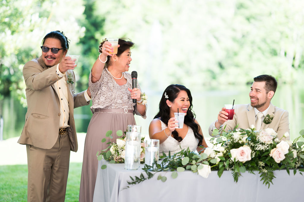 couple raising glass during a toast at their wedding, with bride's parents next to them all raising a cocktail insted of a champagne flute, with big smiles.