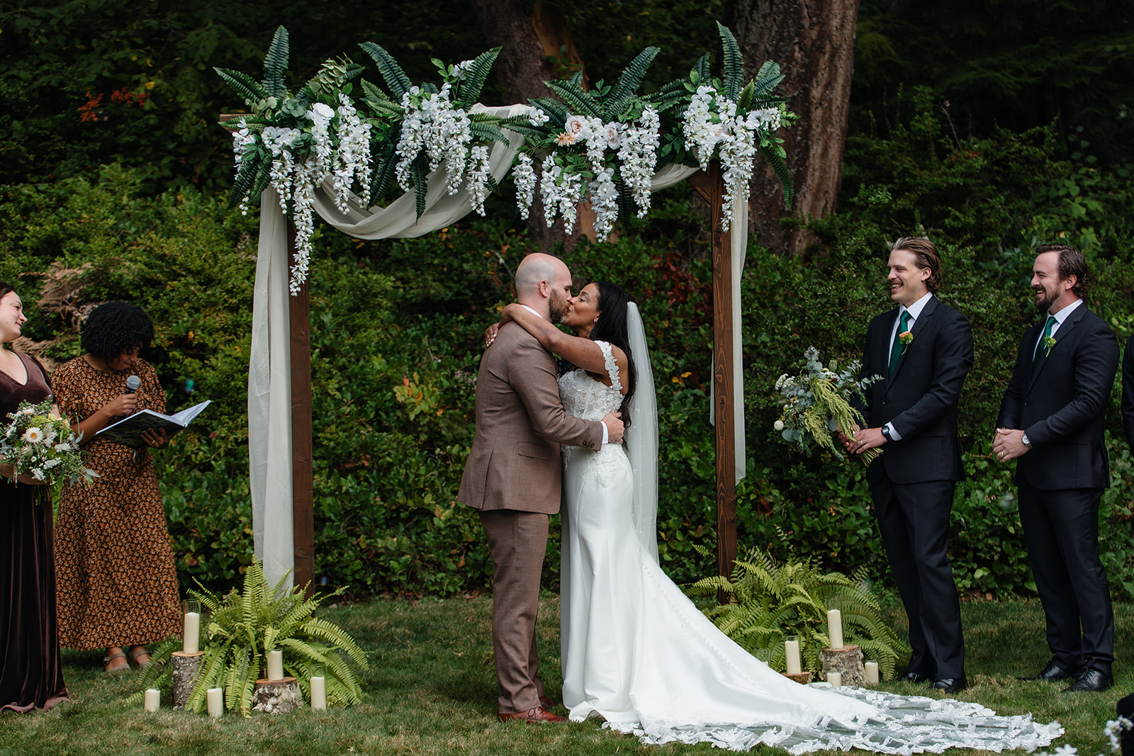couple surrounded by evergreen trees kissing after saying i do at the arbor outside at foxglove lodge